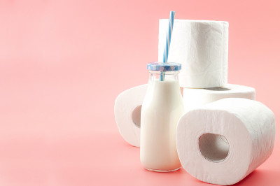 乳糖不耐症和无法消化牛奶的概念主题一瓶牛奶与蓝色的吸管和一卷卫生纸隔离在粉红色的背景与复制空间