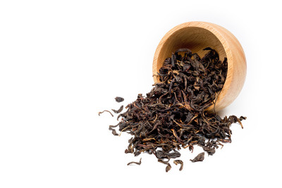 干燥的发酵茶叶从一个铺在白色背景上的木碗里倒出来。