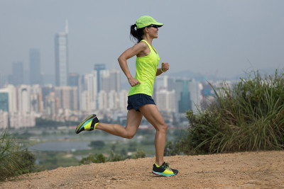 女超级马拉松运动员在现代城市旁边的山上跑步