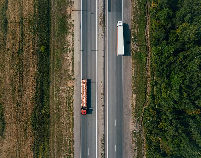 两辆卡车沿着田地行驶在公路上。俯瞰风景