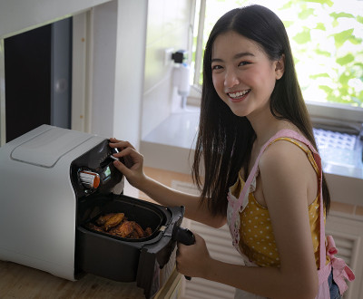 一个亚洲女孩在她家里的厨房里用油炸机烹饪一只炸鸡