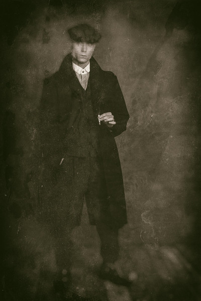 古董湿板照片的男子1920年代英国黑帮穿着黑色外套和扁帽拿着香烟。