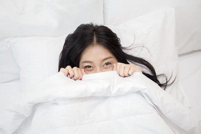美丽的年轻亚洲女人看着相机，而躺在床上，女人醒来的概念，20岁。