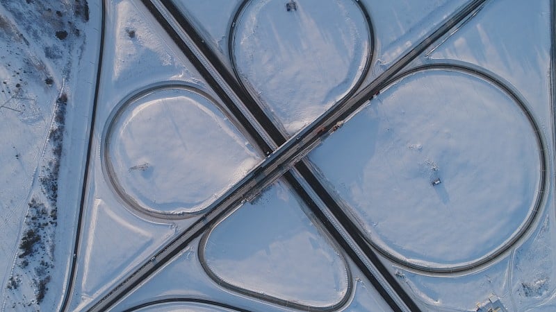 在冰雪覆盖的森林中蜿蜒多风的道路，从上到下的鸟瞰图。