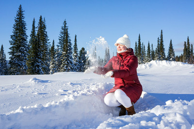 四季。一个穿着红色外套的女孩坐在冬日森林的背景下，抛起了雪。