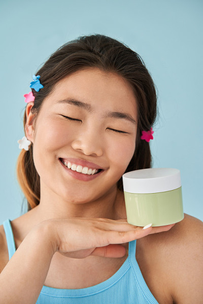 女人在拍摄时闭着眼睛拿着一瓶保湿霜