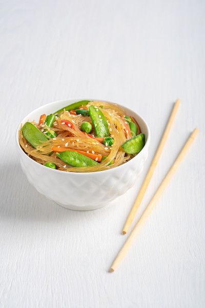 白色木桌上放着亚洲辣日式炒面、青豆和豆角，配以筷子