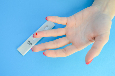 诊断冠状病毒的血液检测。一个修了亮红色指甲的女孩的无名指上有一滴血。刺针手指穿刺，回家快速测试