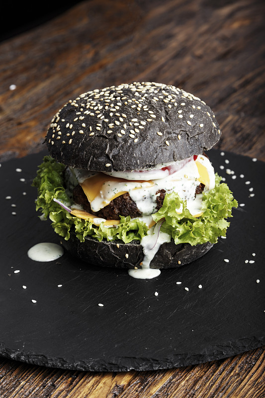 Fresh black burger with meat and vegetables, sprin