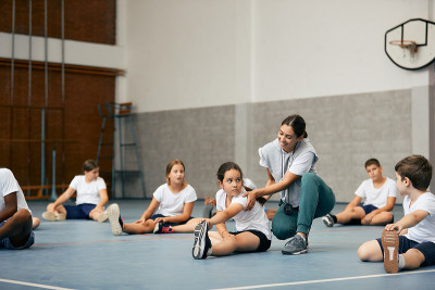 快乐的女体育老师和一群小学生在学校体育馆上课。