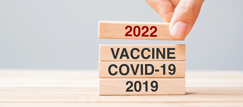 在桌子背景上，手拉着2022块疫苗、COVID-19和2019木质建筑。危机经济、疫苗接种、免疫接种