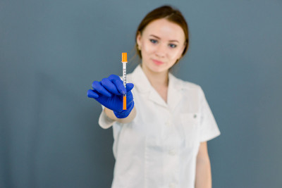 美丽的年轻白种人女医生，美容师拿着注射器与溶液美容注射。孤立的女性工作室肖像在灰蓝色的背景。