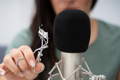 Woman Using Eyelash Curler On Microphone To Make A