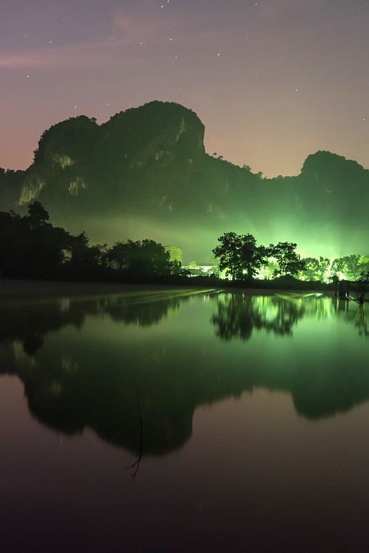 美丽的风景湖泊和山脉在夜晚与星空的背景。山前村庄的照明。日出照在湖面上。夏天的季节。泰国甲。抽象艺术