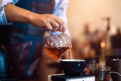 咖啡师拿着蘸汁杯，将蘸汁后的热咖啡倒入一杯咖啡中。