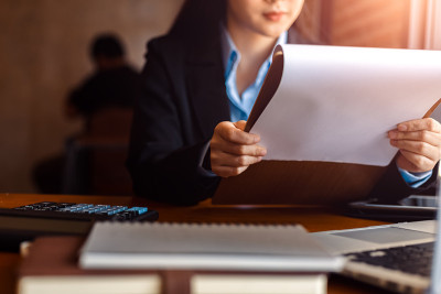 商务女性会拿着文件单阅读以便核对。商业女性工作和笔记本电脑，计算器和书在桌子上。