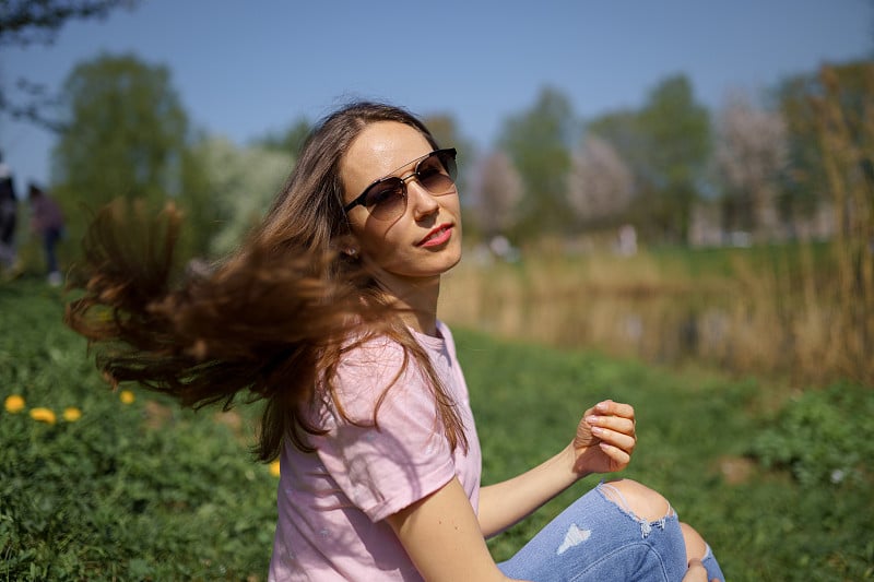 年轻快乐的旅行者棕色头发的女人女孩微笑，转身在一个新的目的地国家与一个粉红色的樱花在波罗的海国家樱花