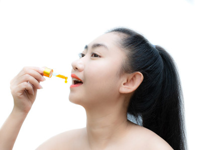 在白色背景下，手持舌下滴管大麻油的女子