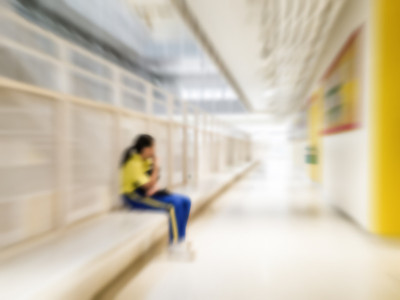 学校观念中的欺凌、歧视和种族主义。模糊的孤独的学生独自坐在走廊上看着智能手机作为网络恶霸。