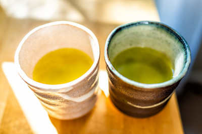 房间里的木桌，早晨的阳光和两个杯子装满了日本充满活力的绿黄茶颜色的早餐容器