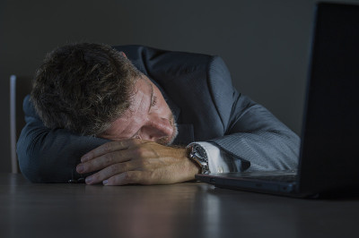 年轻有吸引力的浪费和疲倦的企业家男人睡觉睡到深夜在办公室笔记本电脑书桌上疲惫的金融业务问题和过度工作
