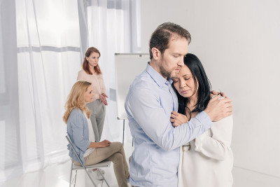 成熟的男人拥抱沮丧的亚洲女人在团体治疗