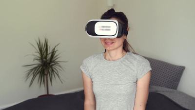 年轻女子坐在卧室里戴着VR眼镜，用增强现实技术进行娱乐、教育、学习和购物