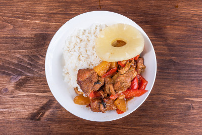 阿多波猪肉，菠萝和胡椒在碗里，煮米饭在一个木制的黑色背景，俯视图