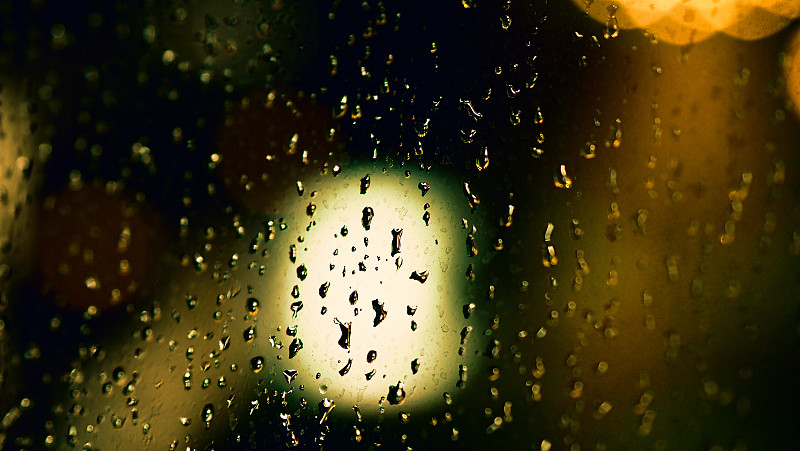 雨点在夜晚落在窗户上。公寓或公寓客厅窗户在雨季的晚上在泰国曼谷。窗外模糊了雨中的城市光线和自然树与天