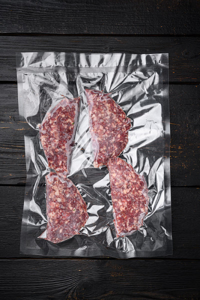 真空牛肉或羊肉排密封密封包装，在黑色木桌背景，俯视图平铺
