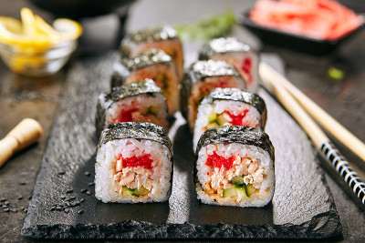 微距拍摄寿司卷在日本餐厅与筷子特写。寿司卷配米饭、炸鲑鱼、飞鱼鱼子酱、黄瓜和辣酱