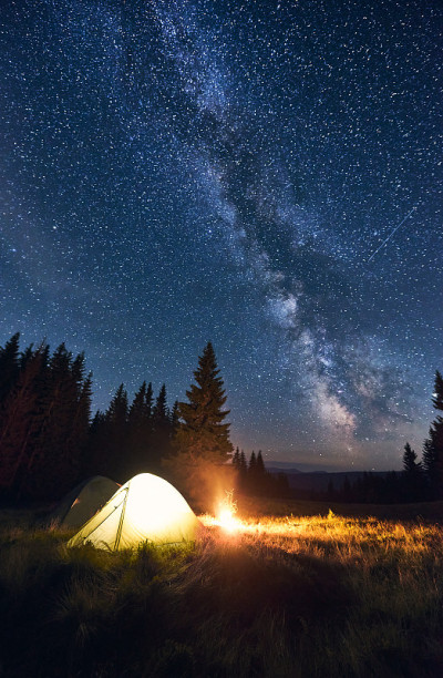 在明亮的星空下，燃烧着的篝火和帐篷，银河系清晰可见。神奇的天空