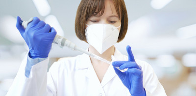 科学家或实验室研究人员戴着防护面罩和实验室手套，手持实验室吸管，将样本移液管入试管。医学诊断、研究和