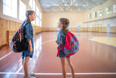空空的学校体育馆里背着书包的小女孩们。