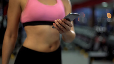 有魅力的女孩在健身房用健身app查手机信息