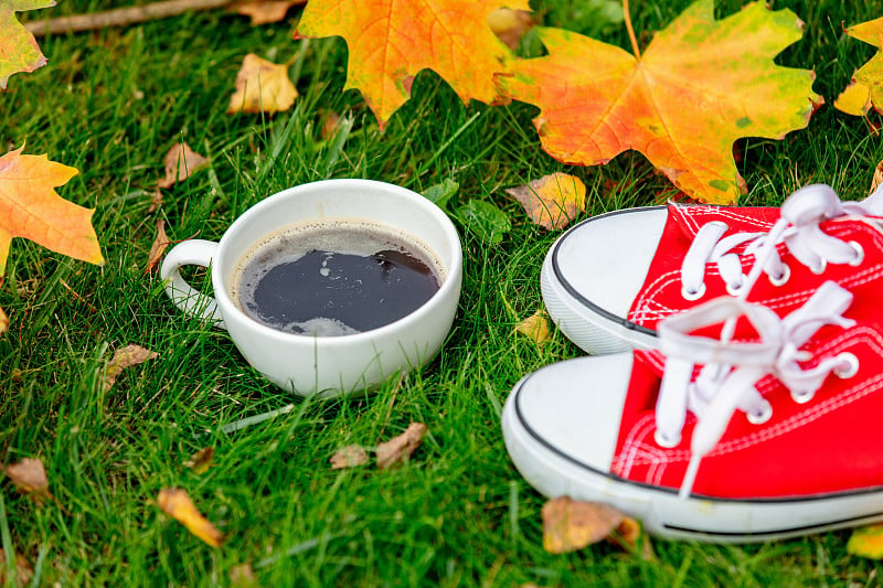 Cup of coffee and red gumshoes with maple leaves