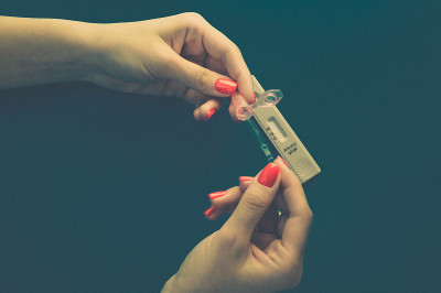 亮红色的指甲在黑色的背景上。拥有时尚美甲的女孩手持医用柳叶刀。快速诊断疾病。家庭医疗检测检测疾病
