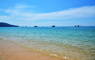 海景-空旷的热带海滩，清澈的水和一些渔船在地平线上晴天。泰国甲米省的蓝色海水和金砂。