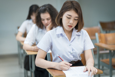 选择性焦点的青少年大学生坐在讲座椅上做期末考试和写在试卷上的答题卡在教室里。大学生在教室里穿制服。