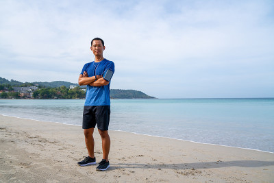 夏日清晨，身着运动服的亚洲男子在沙滩上慢跑。