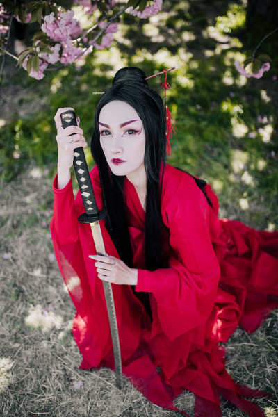 一名年轻女子在盛开的樱花旁手持日本武士刀扮演艺妓。