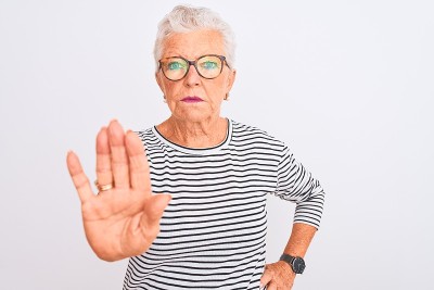 年长的灰白头发的女人穿着条纹海军蓝t恤眼镜在孤立的白色背景做停止唱歌与手掌。警告表情与否定和严肃的手