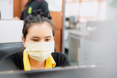 戴口罩的亚洲妇女在居家隔离中使用笔记本电脑工作、使用在线电信、保持社交距离