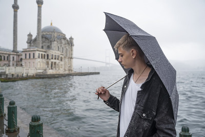 少年少年拿着伞看着暴风雨笼罩的城市，恶劣的天气，下着雨，倾盆而下