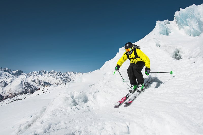 专业滑雪者在冬季从冰川上跳跃前的速度对着蓝天和高山