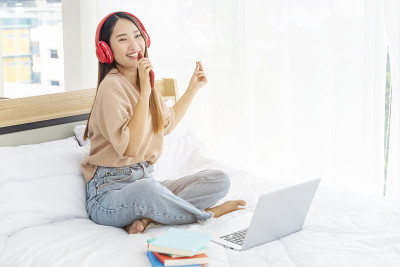 放松女人拿着书在床上用耳机听音乐。少妇放松阅读，翻开书本，休闲心灵。幸福美丽的女人人
