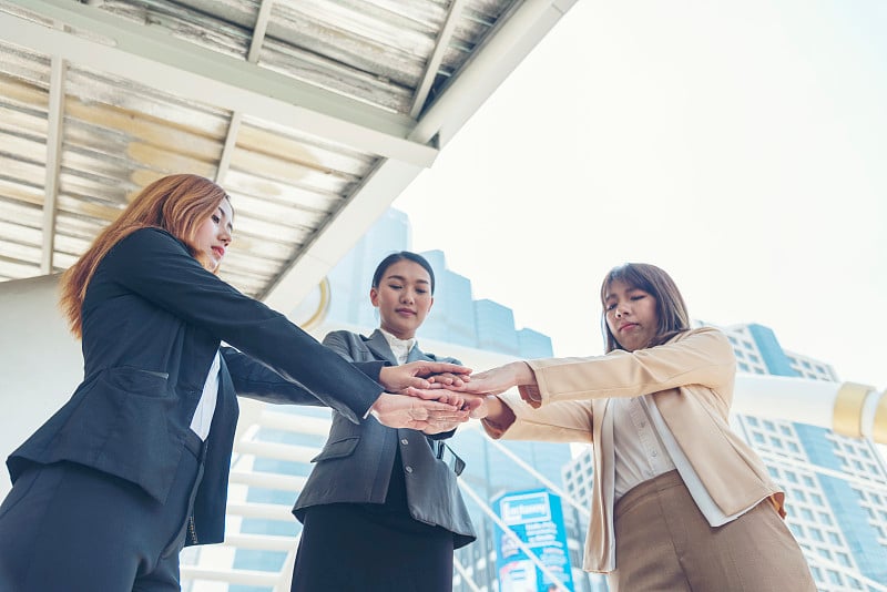 女性伙伴们在现代城市户外携手团队商务人士聚会。女性之手加入授权伙伴团队连接社区。兼并收购伙伴关系