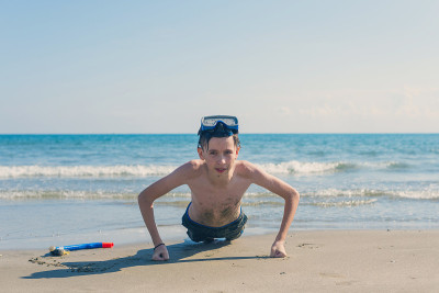 13岁的男孩在海滩上拧着潜水面罩和潜水管。旅游和夏季概念。