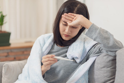 一名年轻亚洲女子在用电子体温计测量体温时，感冒发高烧。