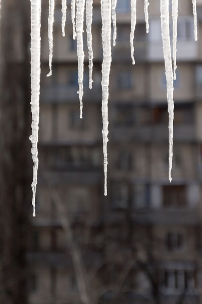 危险的冰柱悬挂在满是积雪的屋顶上。冬季小镇的街道上有巨大的冰柱